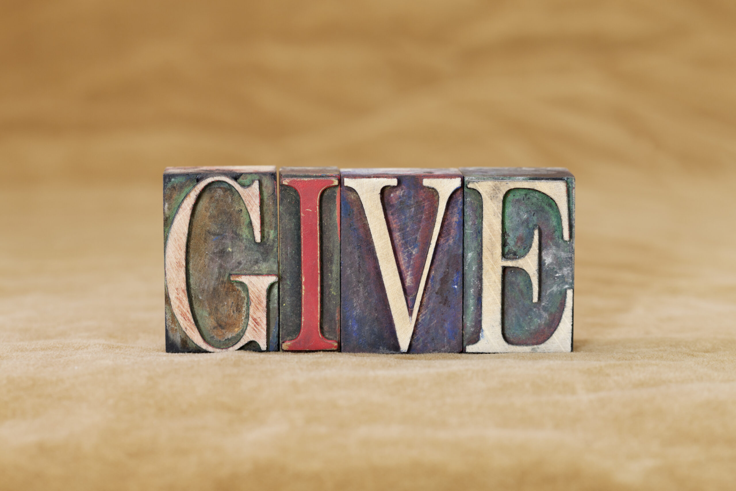 Typesetting blocks spelling out GIVE, on a tan background. Charitable Giving in a High-Income Year.